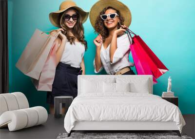 Two happy girl friends in straw hat and sunglasses with shopping bags at blue studio background, copy space, Black friday, sales. Wall mural